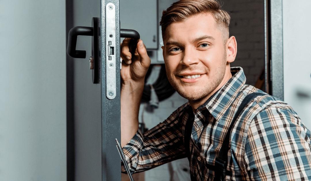 Smiling man in a plaid shirt stands at an open metal safe, holding a tool in his hand (professional locksmith/technician).
