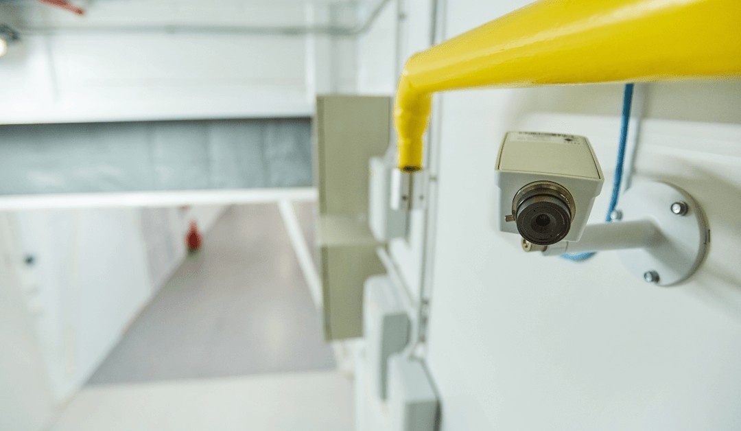 Security camera mounted on a bright yellow railing in a hallway, monitoring the area.